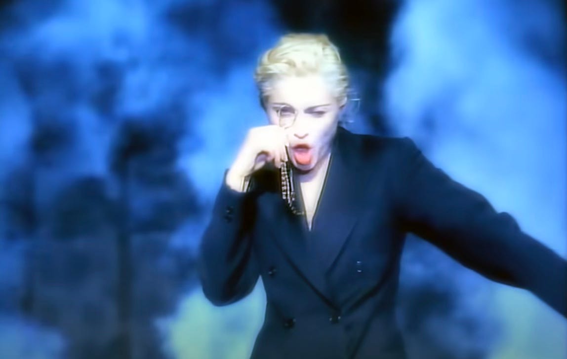 Madonna dances in a suit and peers through a monocle