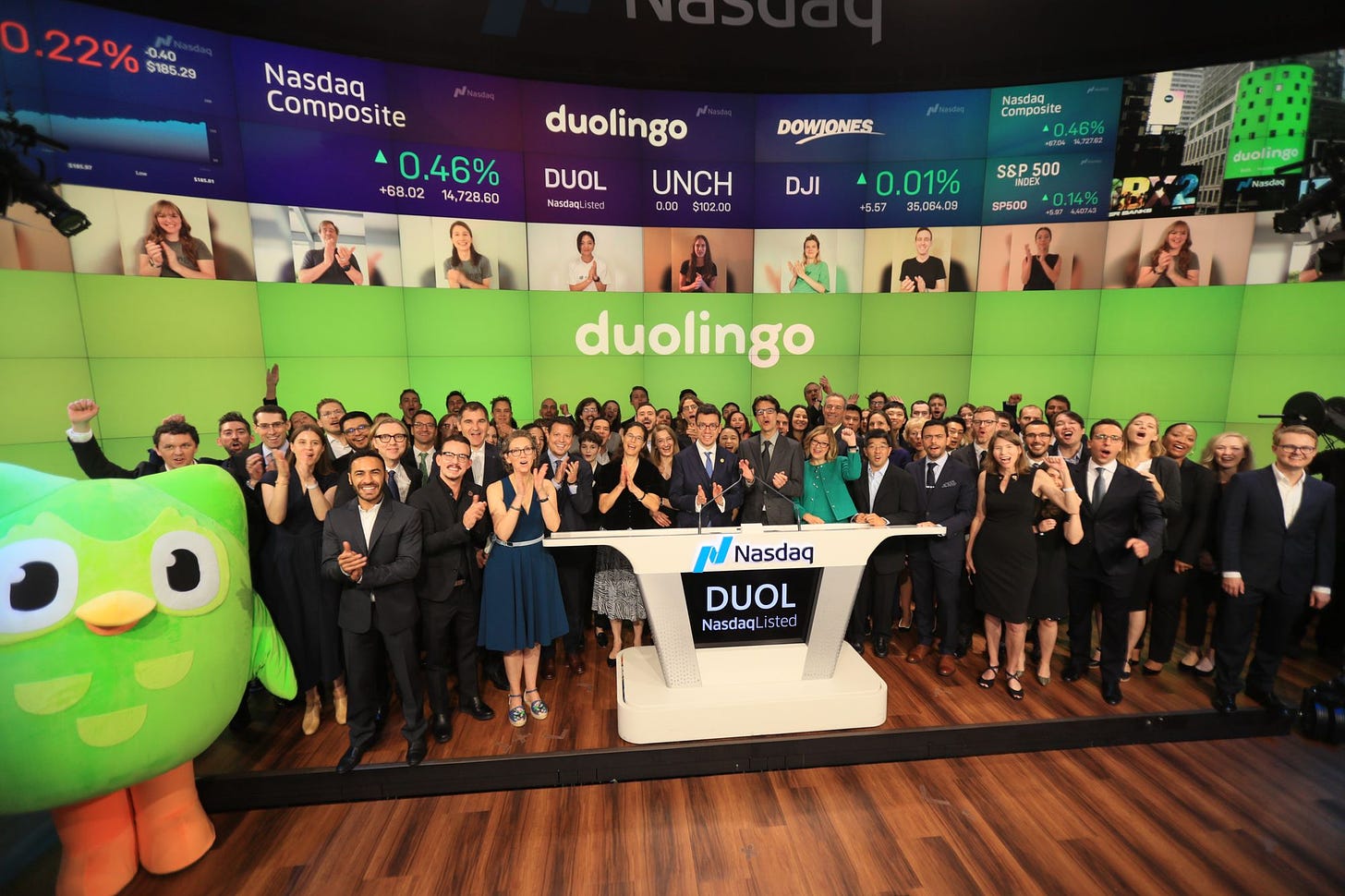 photogrpah of blog post author and Duolingo co-founder and CEO, Luis von Ahn, standing with a group of ~100 Duolingo employees and the green Duolingo owl mascot at the Nasdaq podium which is labeled "DUOL".