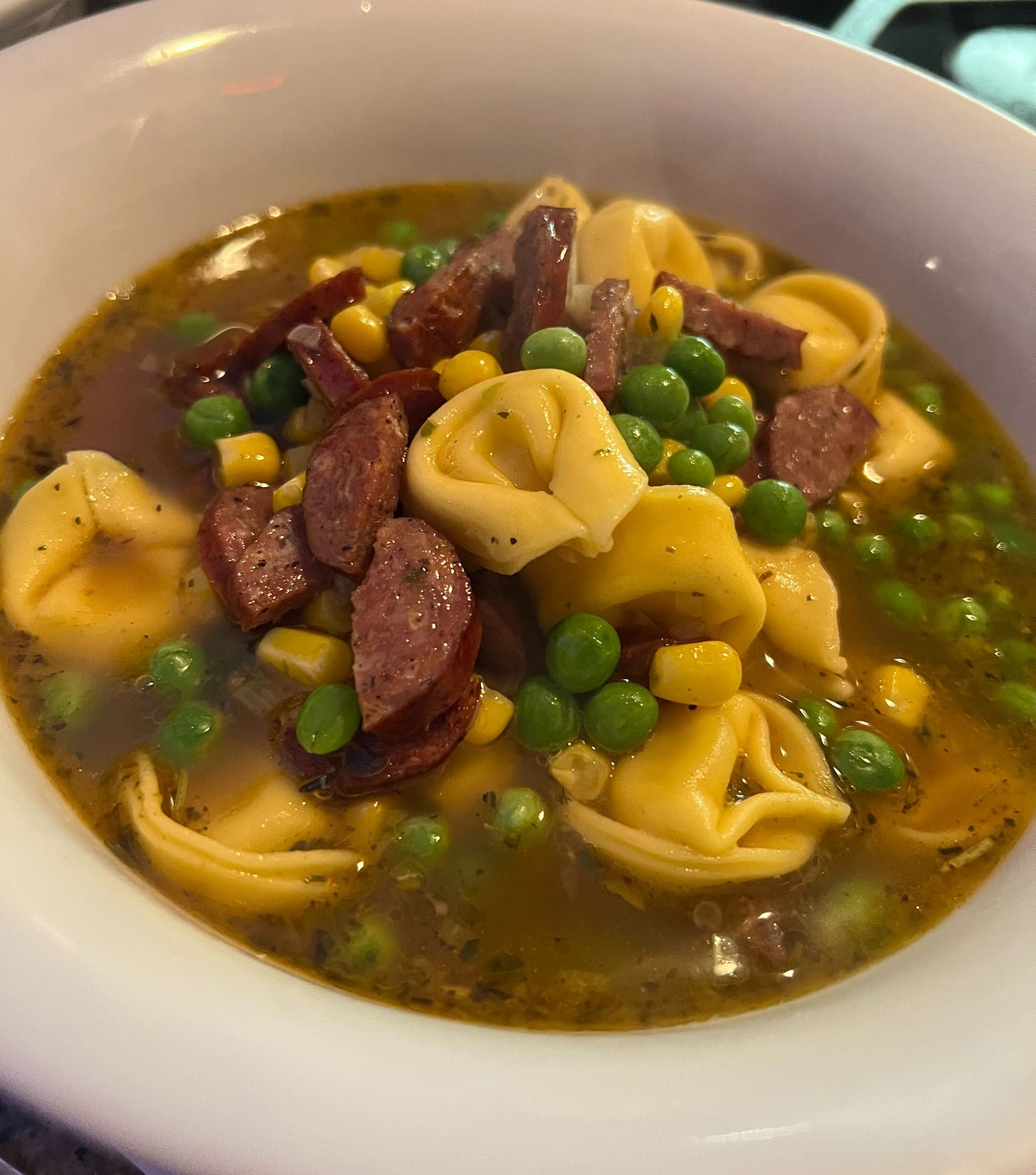 tortellini soup with peas, corn and sausage in a white bowl