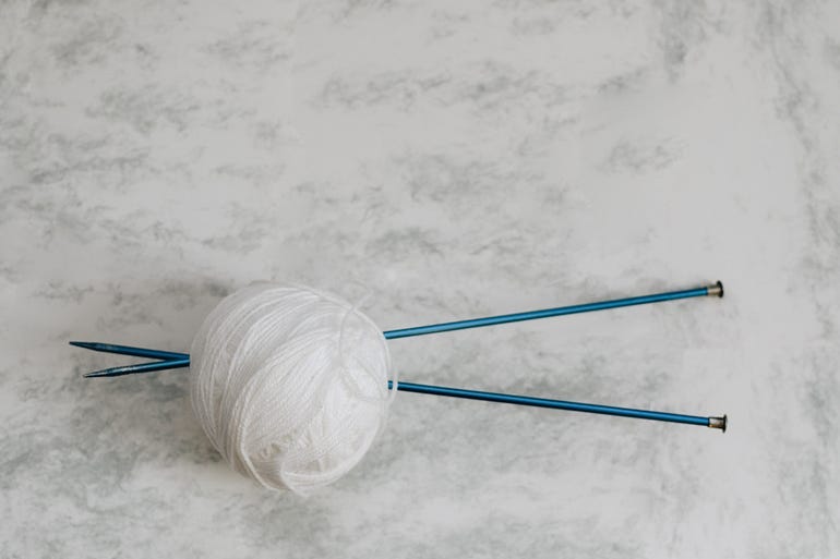 Two turquoise colored knitting needles stuck through a ball of white yarn.