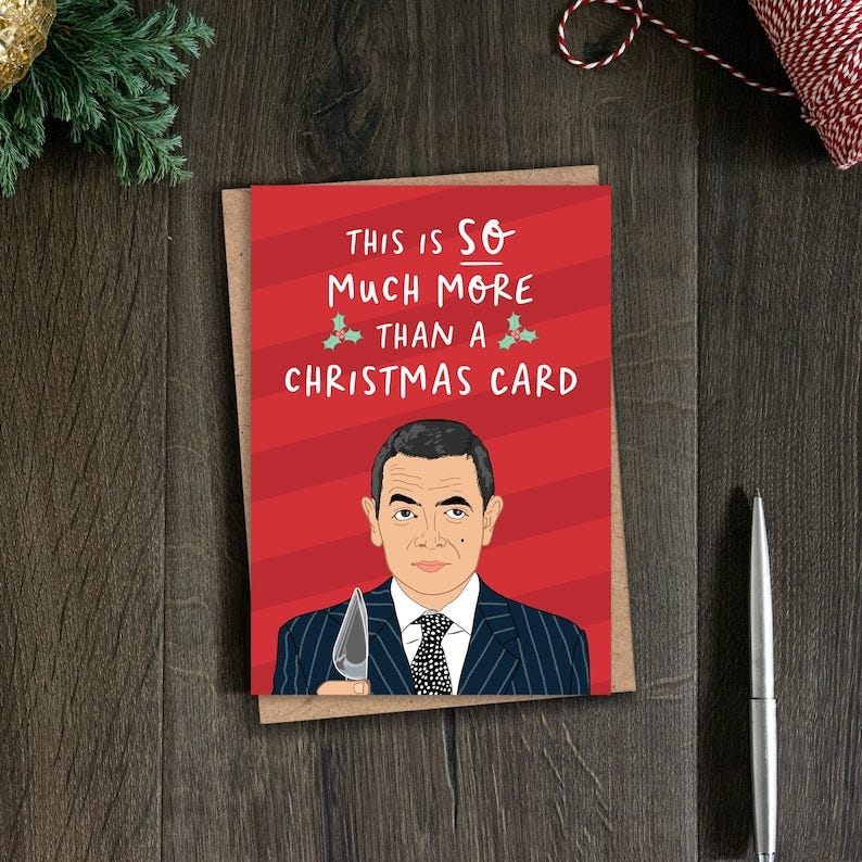 May include: A red and white Christmas card with a cartoon image of Mr. Bean holding a knife. The text on the card reads 'This is SO much more than a Christmas card.'