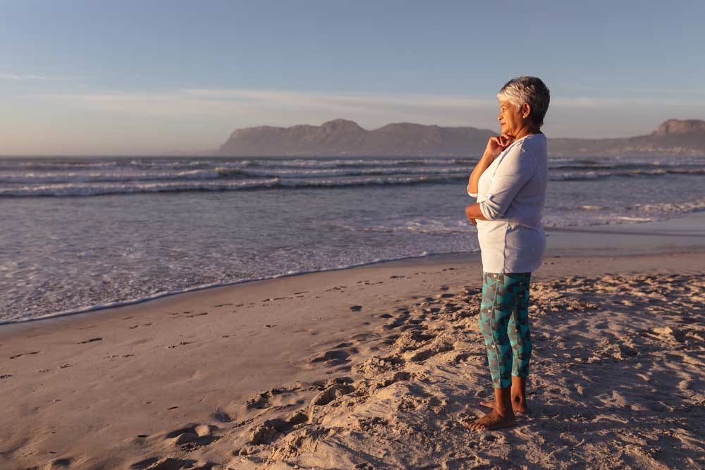 Thoughtful senior woman contemplating the past while standing on the beach.