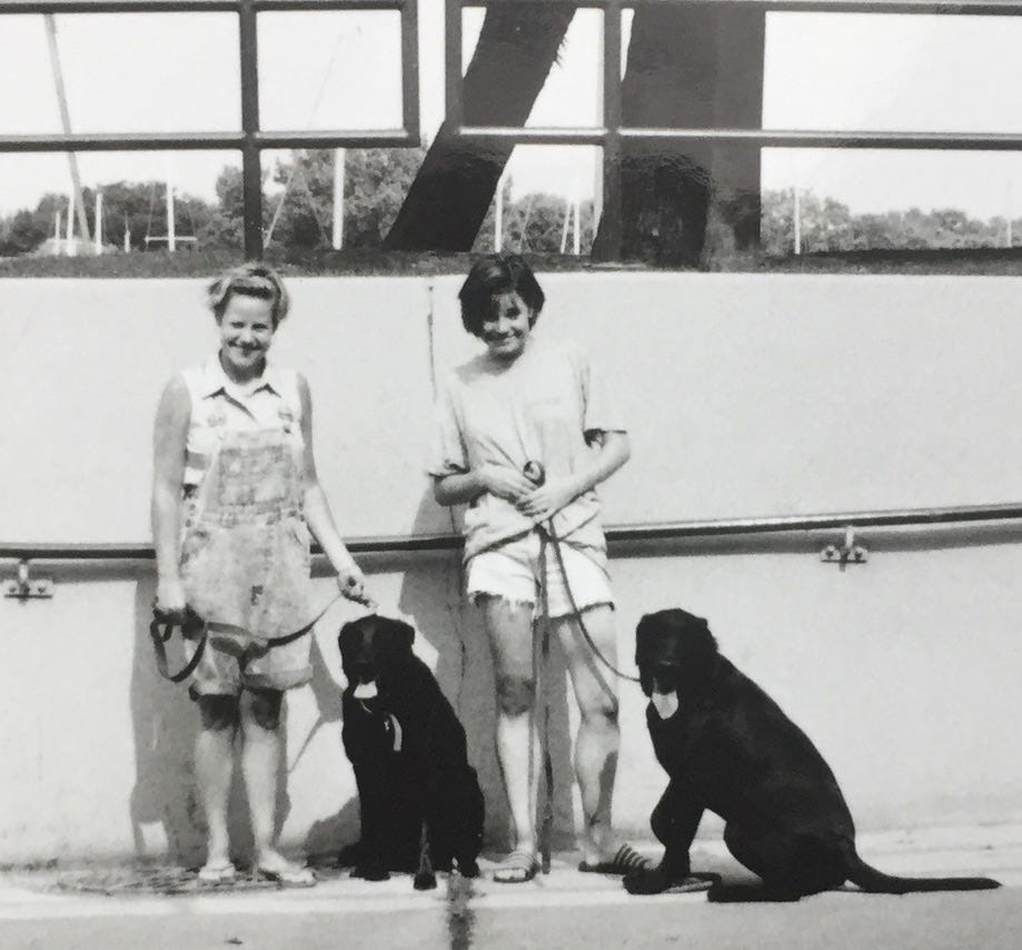 Two sisters with their black labradors on leashes 
