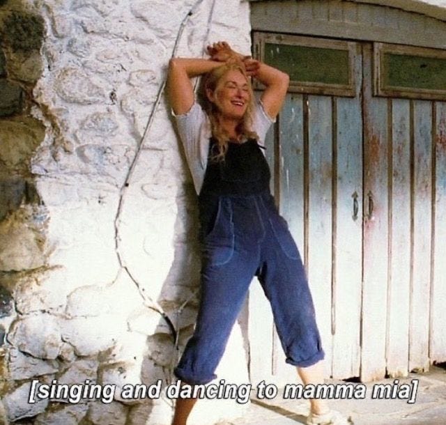 This may contain: a woman leaning against a stone wall with her hands on her head and the words singing and dancing to mama mia