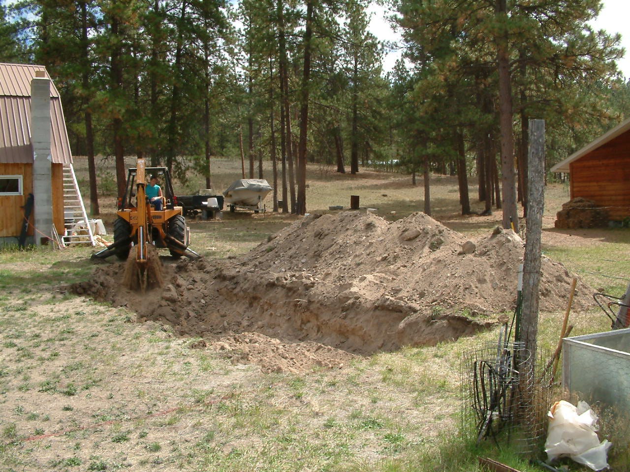 left to right, the side of a barn, a tractor digging a hole in the ground, and the side of a house