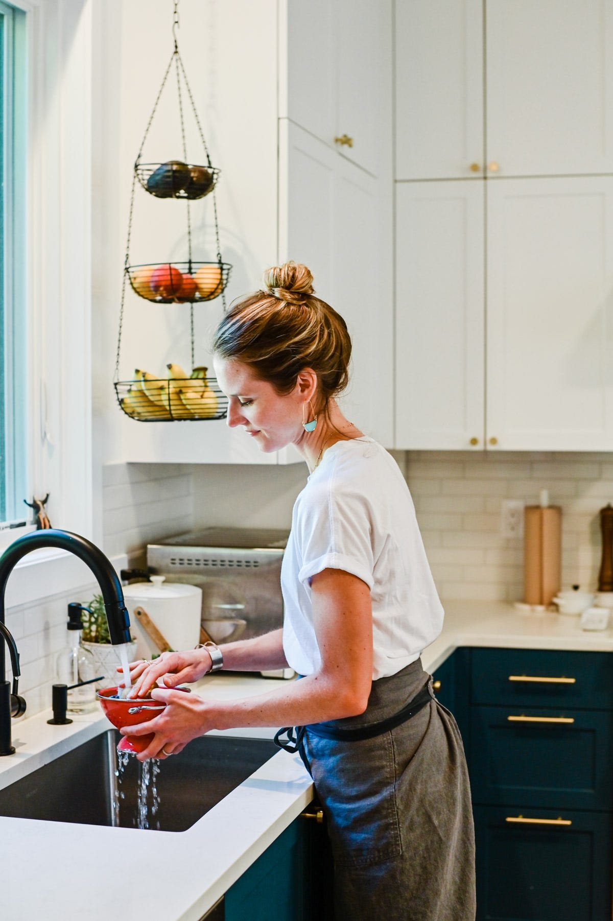 Nicki, rinsing food in a small red colander under the tap in her kitchen.