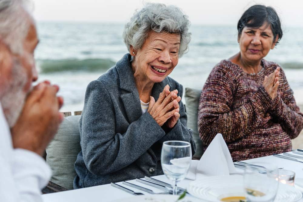 Senior friends enjoying an outdoor dinner party together on the beach.