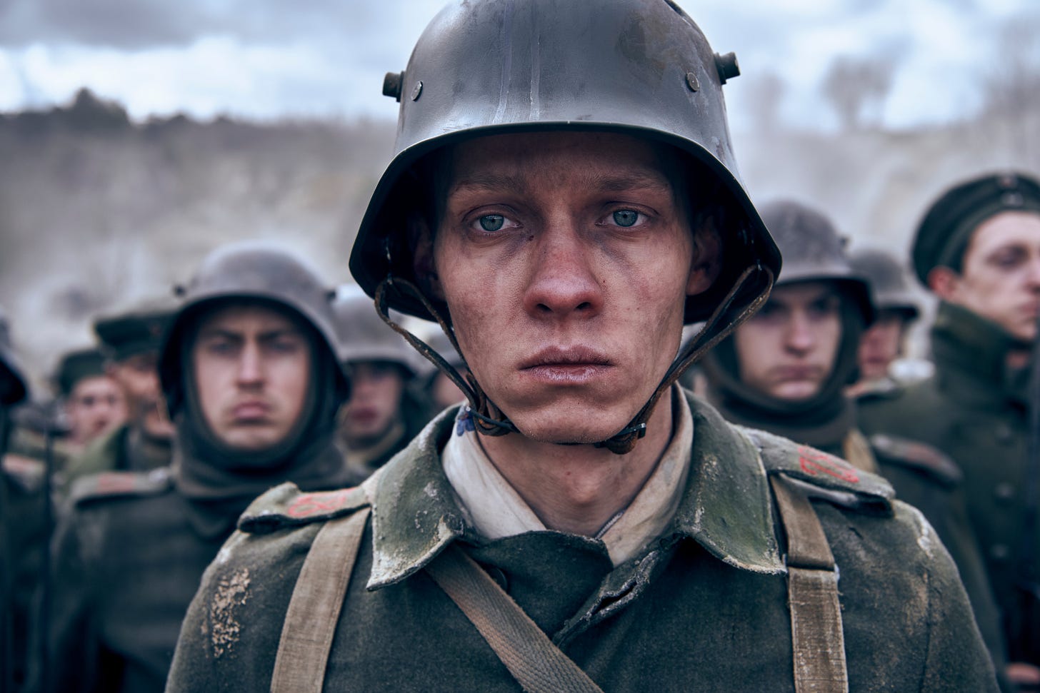 A white, blue-eyed young man with a gaunt face wears a WWI-style German uniform and bucket helmet.