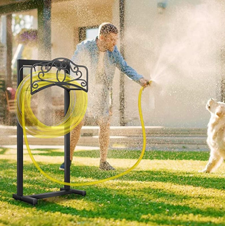 Hose holder with yellow ghost hose being held by a man in a jacket and shorts; he seems to be spraying but there is no nozzle and the overspray is going all over his backyard and an excited golden retriever