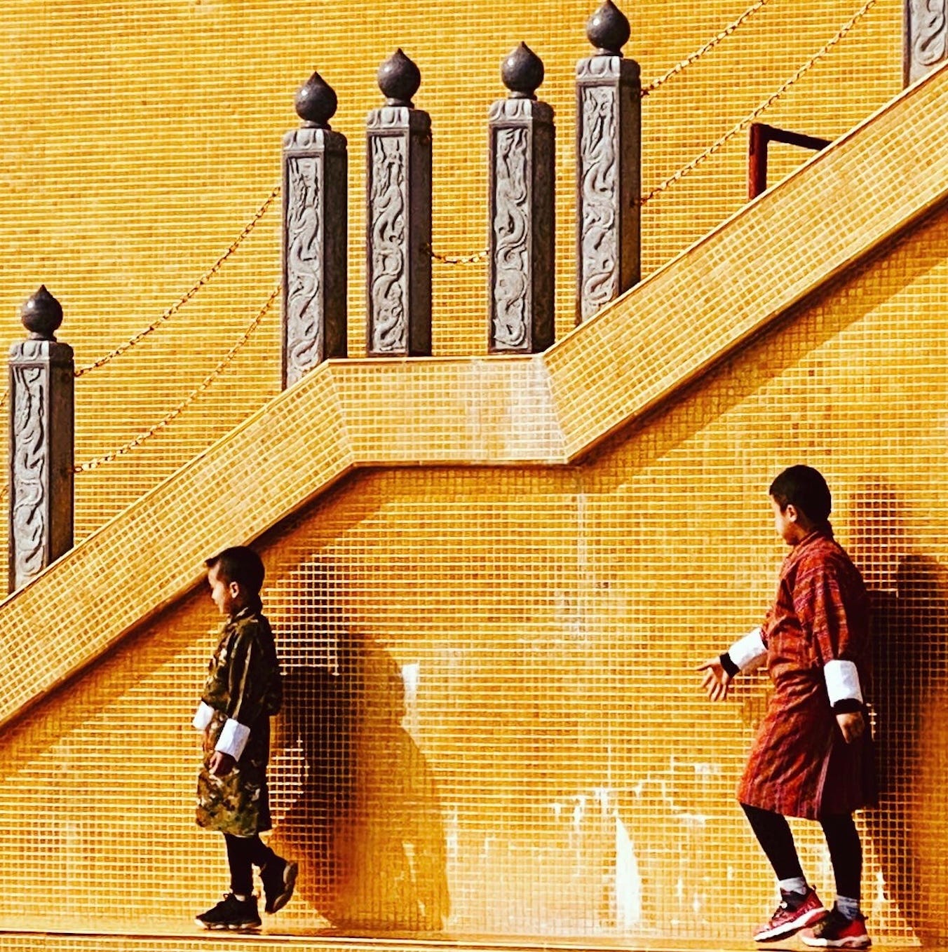Two young boys, dressed in traditional robes, walk past a gold temple.