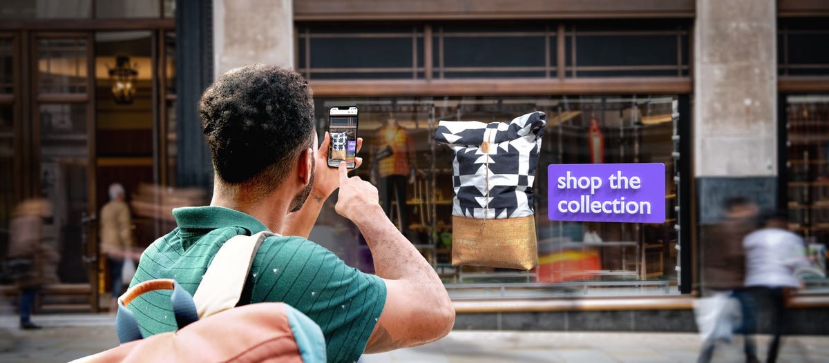 Someone in front of a store holding up a phone to look through a camera