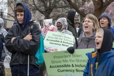 Blind, low vision, and sighted protestors of all ages shout passionately in the rain during Show Me the Money: Marching Together for Accessible and Inclusive Currency on Friday, March 10, 2023 in Washington, DC