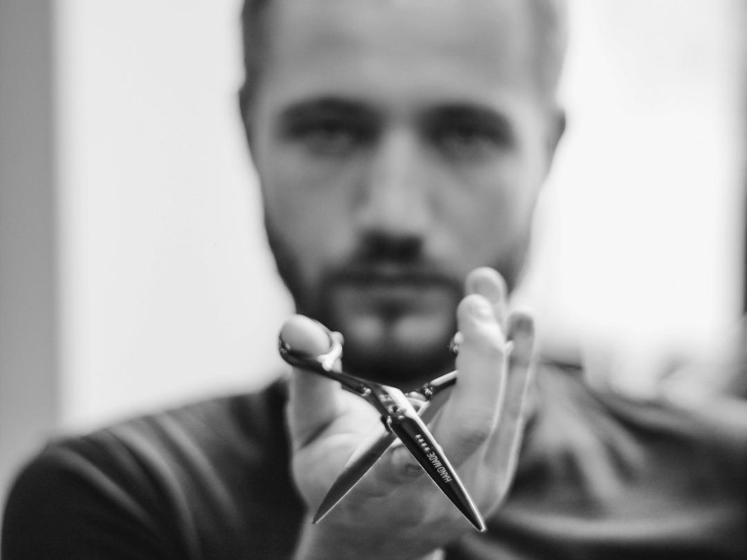 shallow focus photo of man holding scissors shallow focus photo of man holding scissors