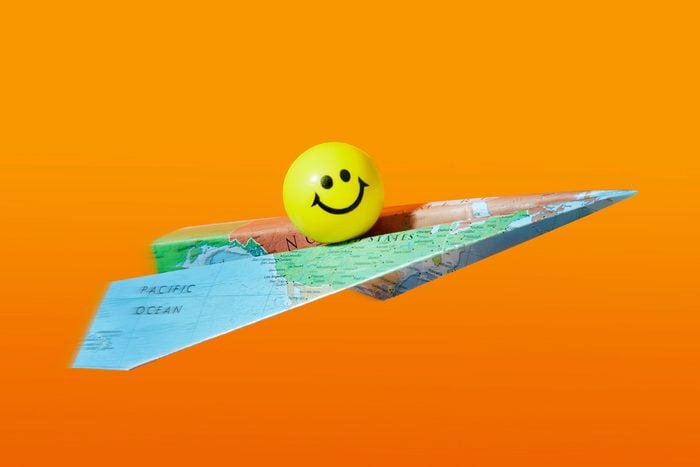 Smiley yellow ball riding On A Paper Airplane made from a map; orange background