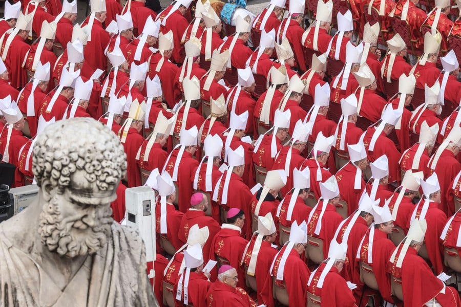 Dozens of red-robed cardinals sit in rows.