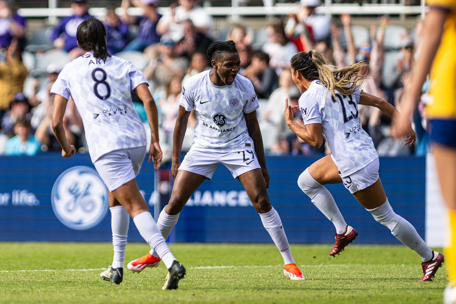 Three players in white and purple uniforms on a soccer pitch