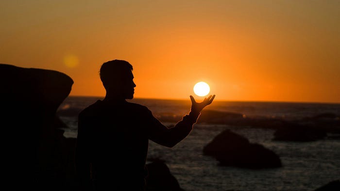 Person watching the sunset and appearing to hold the Sun in his hand.