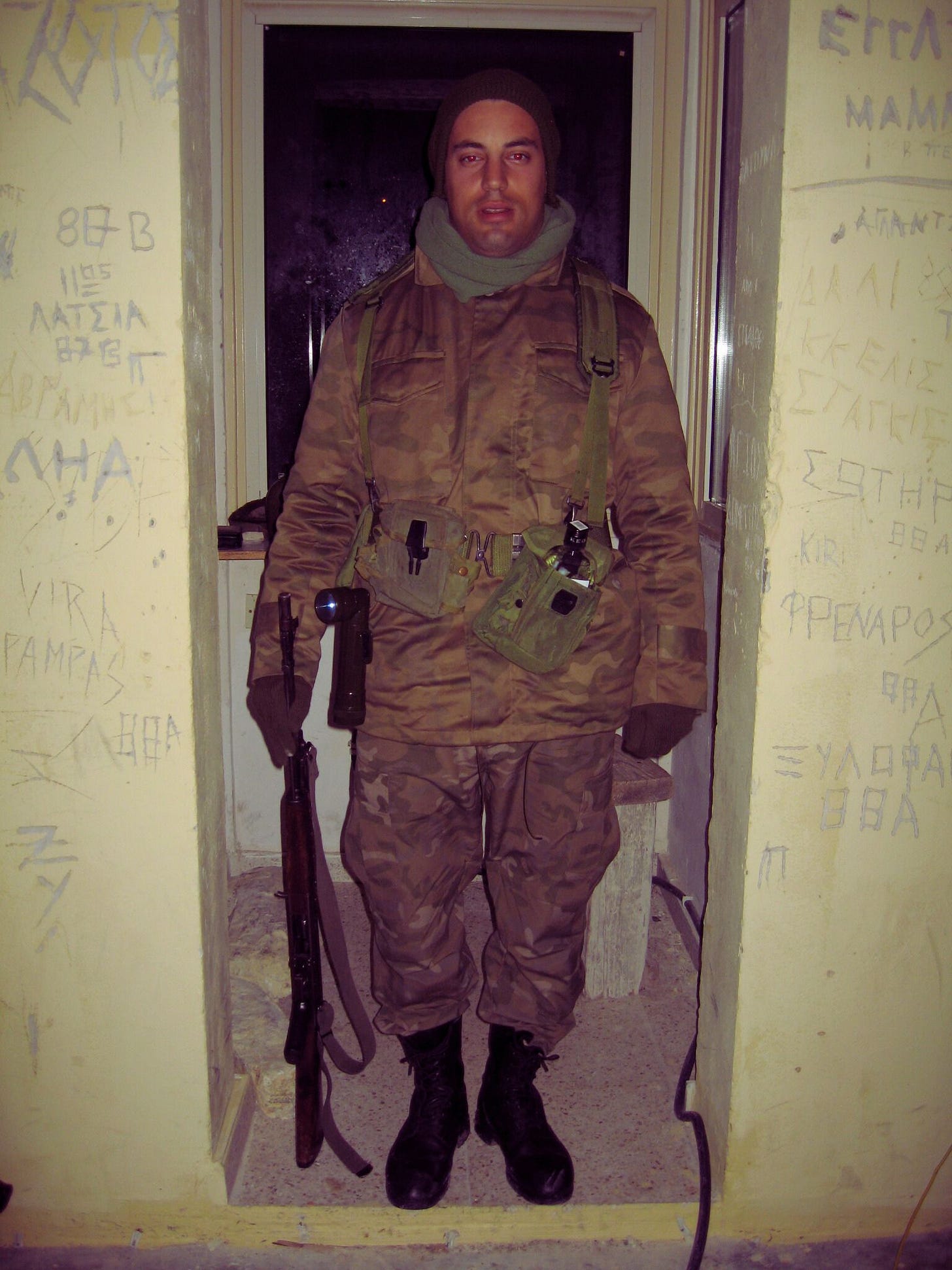 a cypriot conscript standing in front of a door in a tiny room 