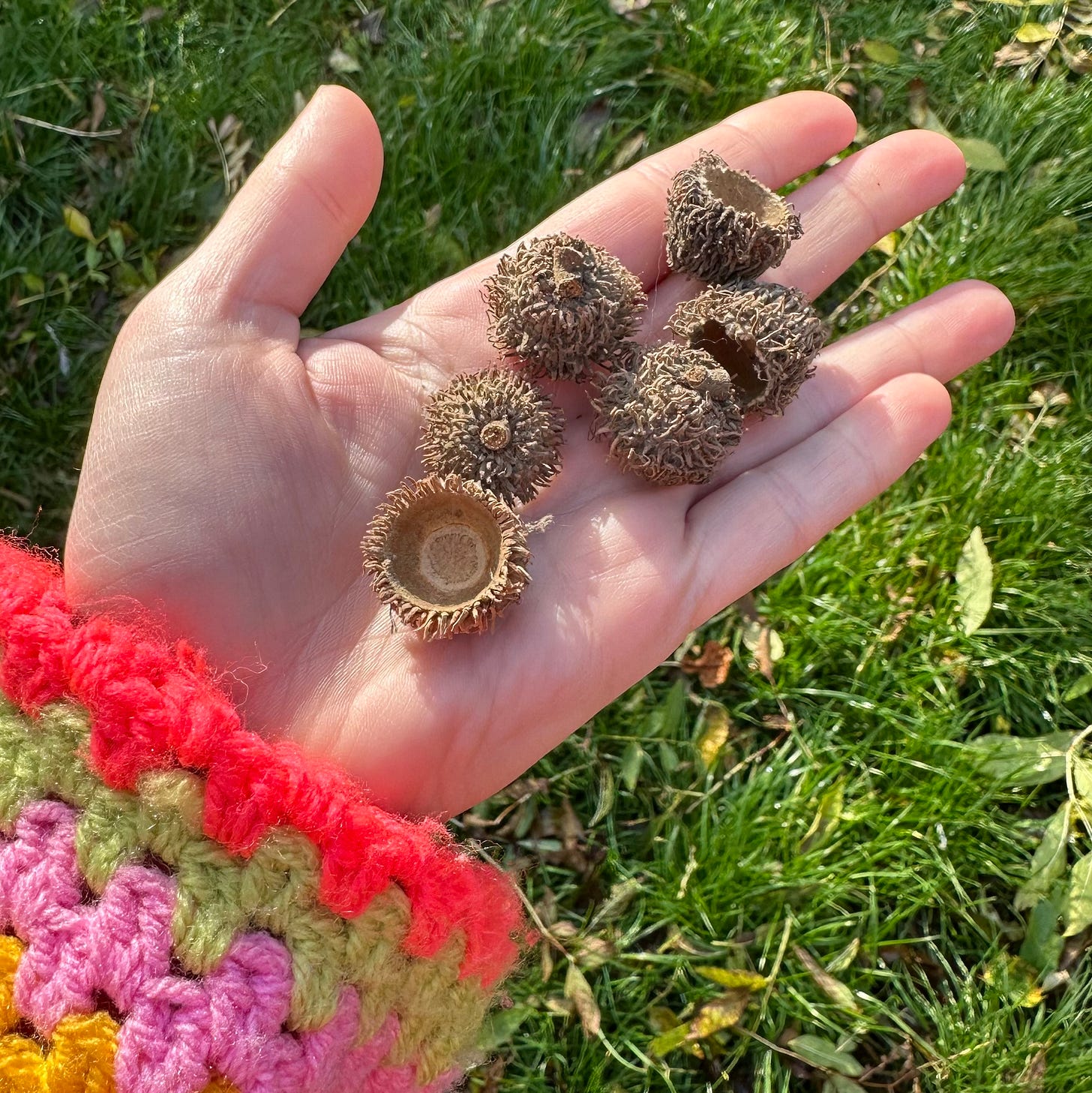 A hand and arm with colourful crochet cardigan showing a selection of tops from an unidentified