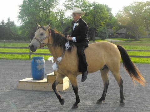 Man in a tuxedo and wearing a cowboy hat riding a horse bareback