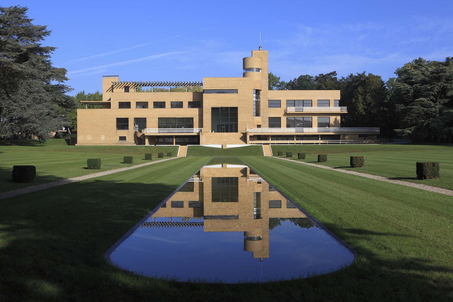 Photo shows a south view of Villa Cavrois in France, designed by Robert Mallet-Stevens. This is a modernist mansion house, with minimal styling and a long rectangular lake stretching towards the foreground.