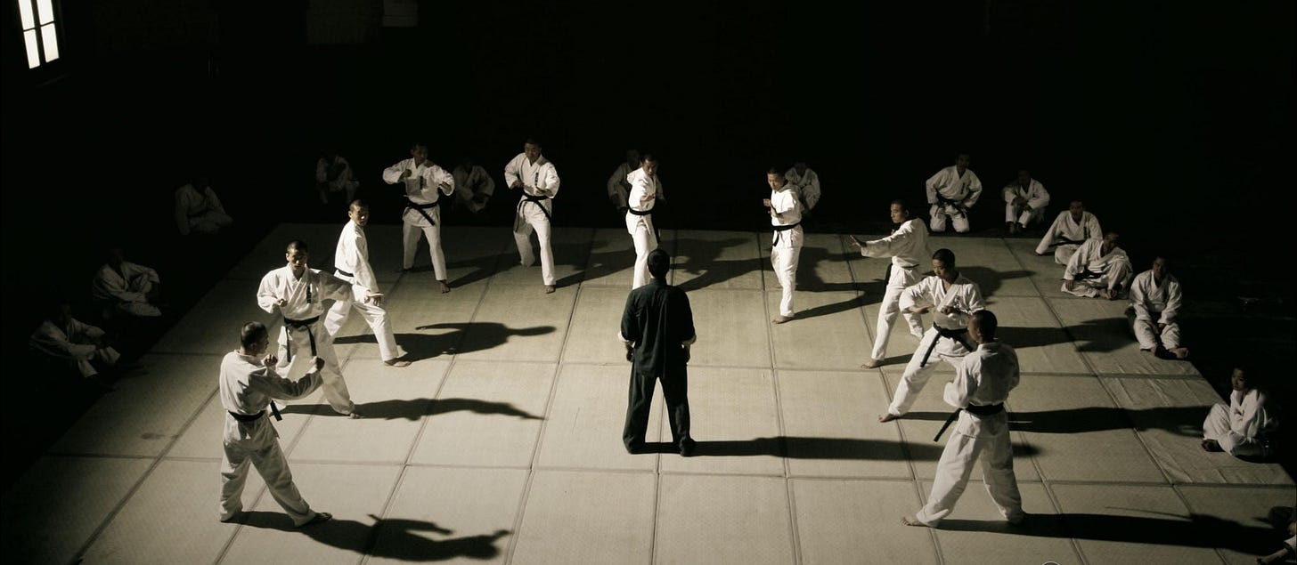 Ip Man stands in the middle of a martial arts stage surrounded by 10 opponents.