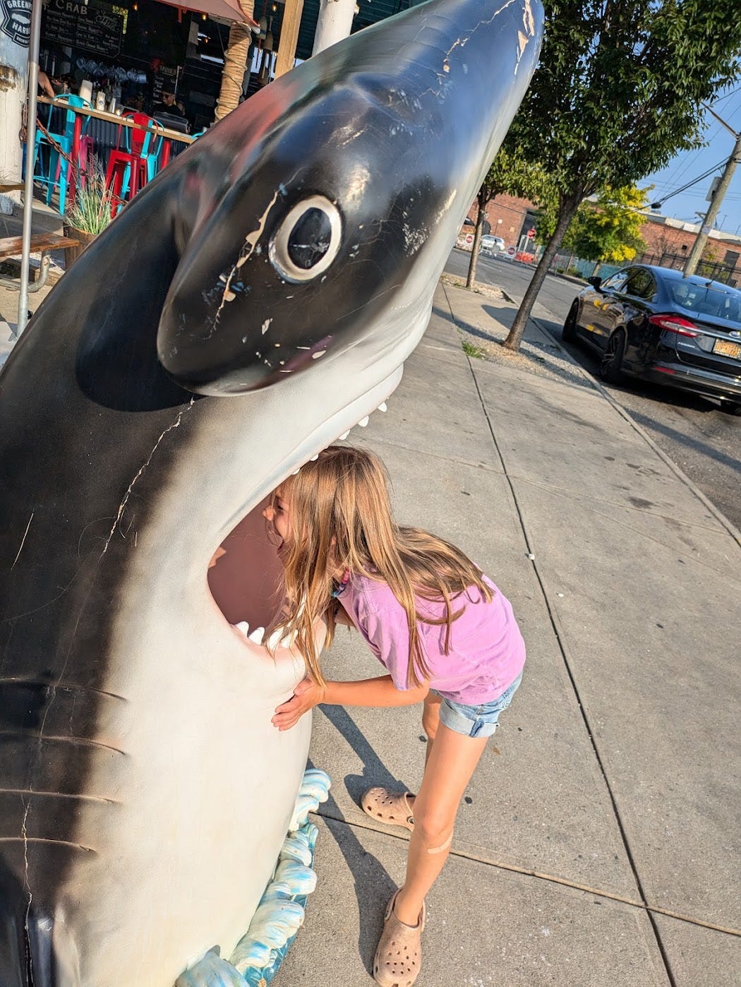 A girl in a purple outfit sticks her head in a shark sculpture