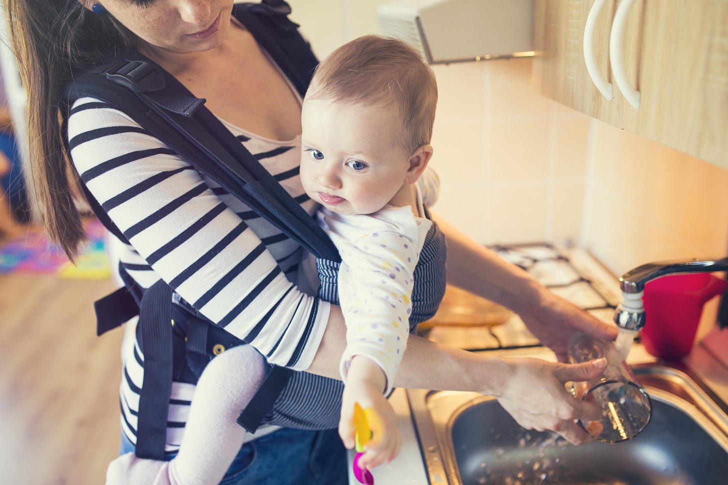Woman at a sink with a baby strapped to her