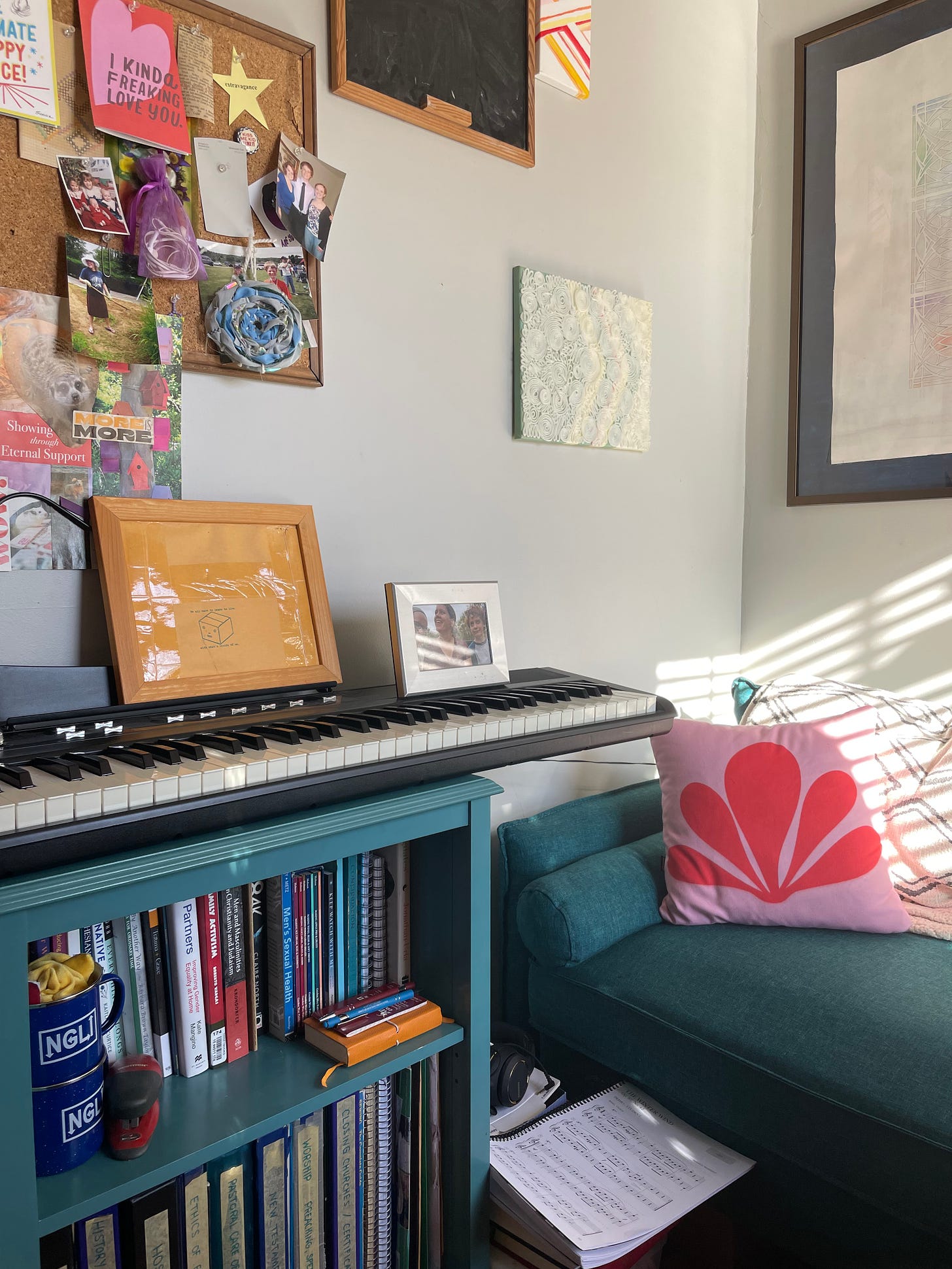 A keyboard sits on a blue bookshelf.  There is a color array of cards on a corkboard above it and a matching blue loveseat to the right.