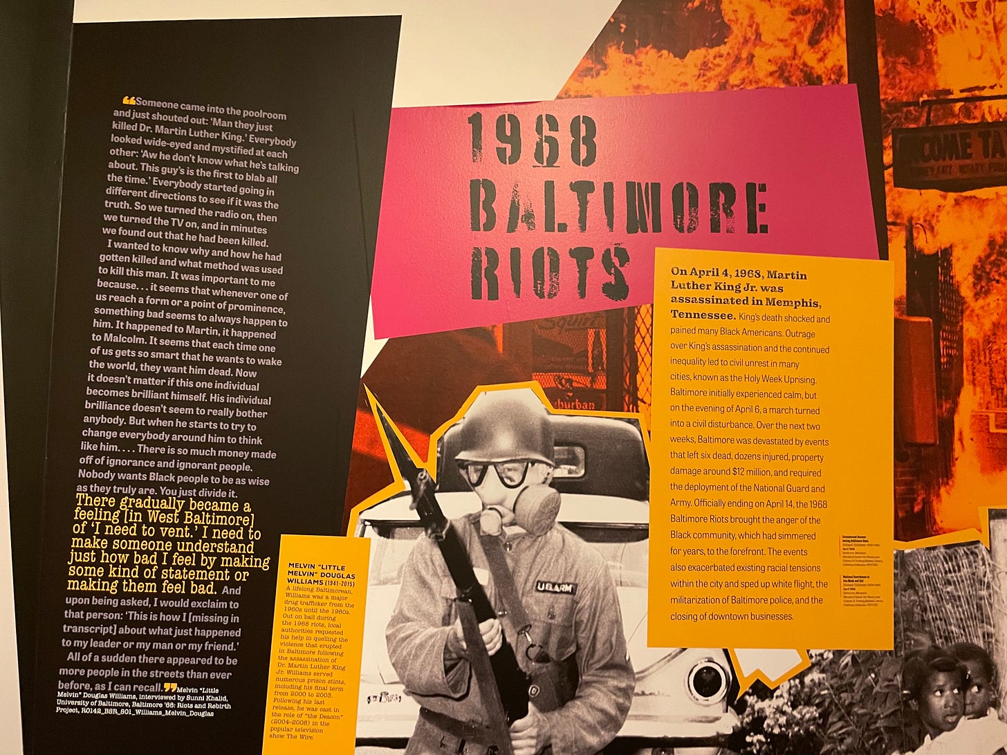 A series of museum display panels with the text heading “1968 BALTIMORE RIOTS.” Accompanying images include flaming buildings and a person dressed in riot gear.
