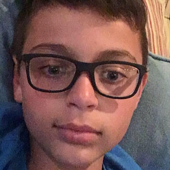 An apparent selfie of a young boy, wearing glasses, with his head on a blue pillow