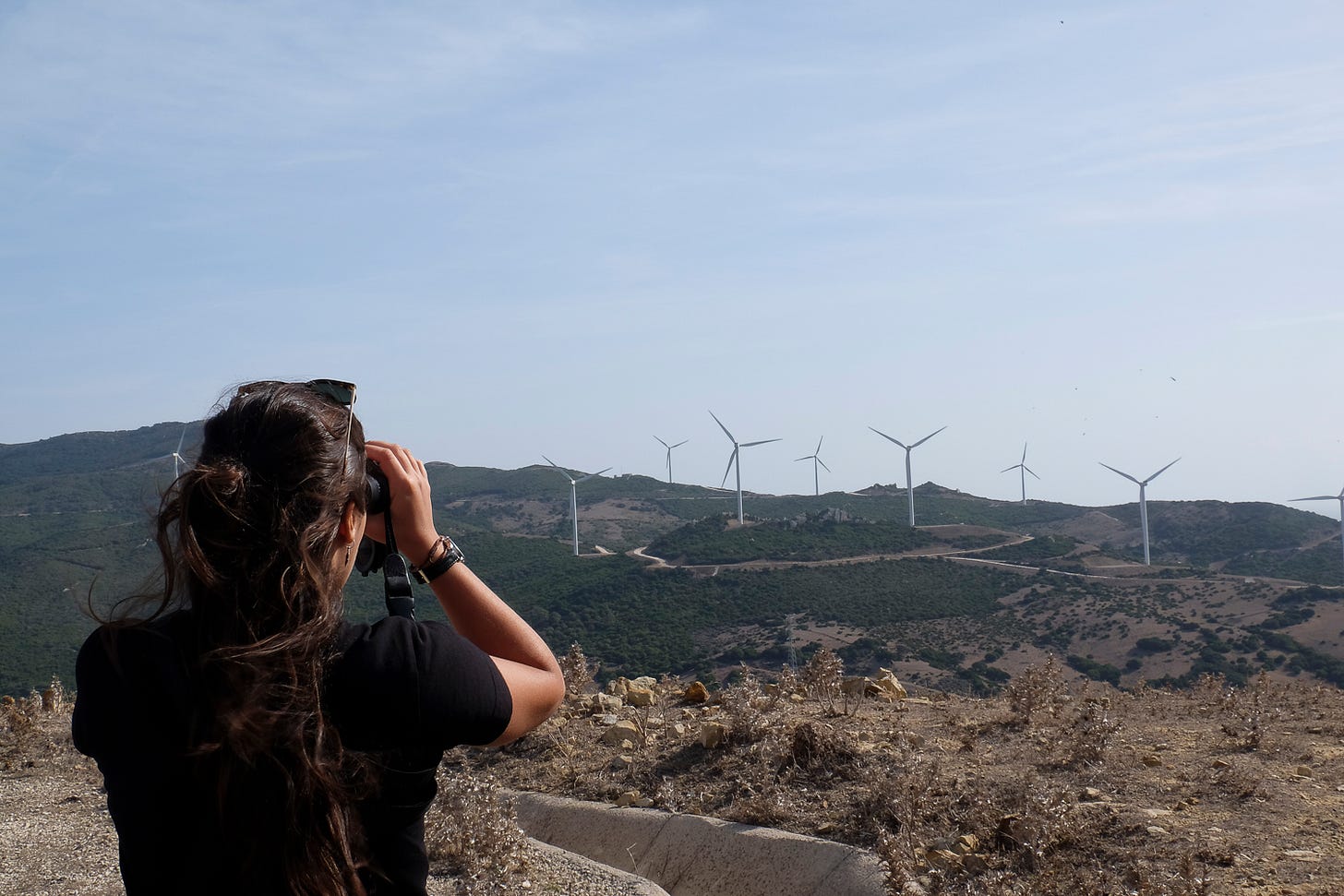 Woman looks through binoculars towards wind turbines