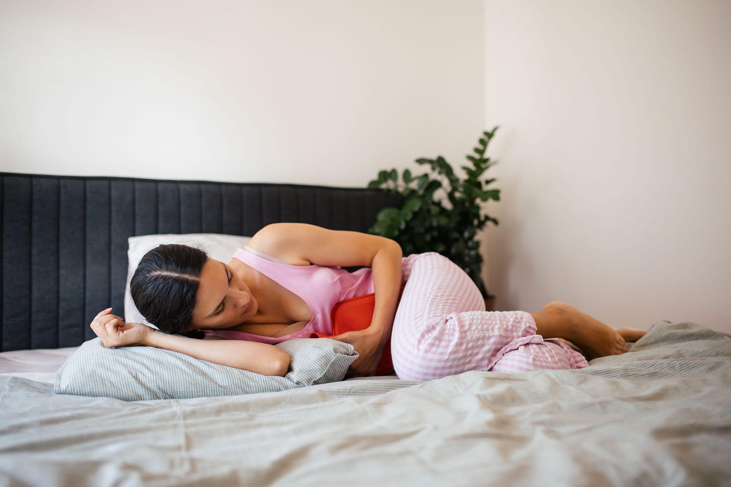 Woman laying in bed with a hot water bottle on her stomach 