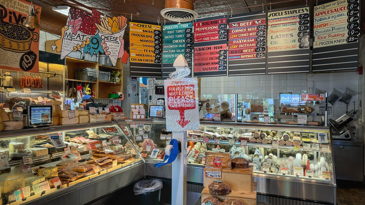 The deli and cheese counters at Zingerman's deli. The cases are teeming with product. There are hand-drawn signs above giving prices. It's a glorious jumble. 