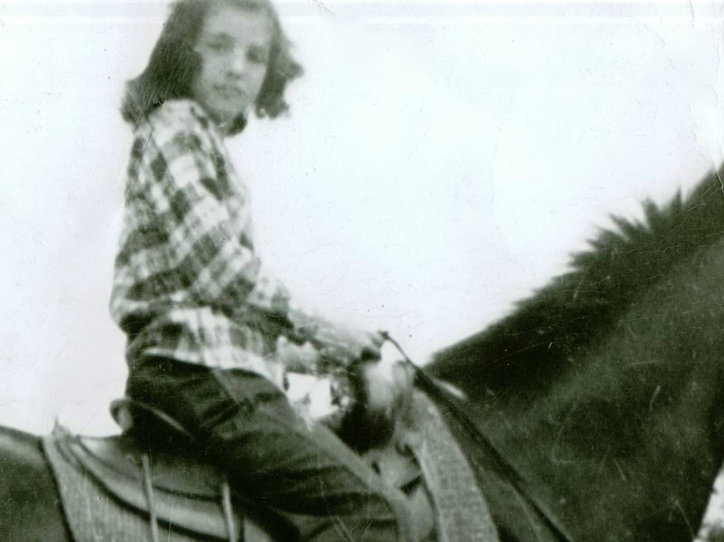Marlee, wearing a plaid shirt and jeans and looking at the camera, doing what she loved the most, riding a horse. This was taken a short time before she was struck with polio. Wearing a plaid shirt and jeansSitting on a horse
