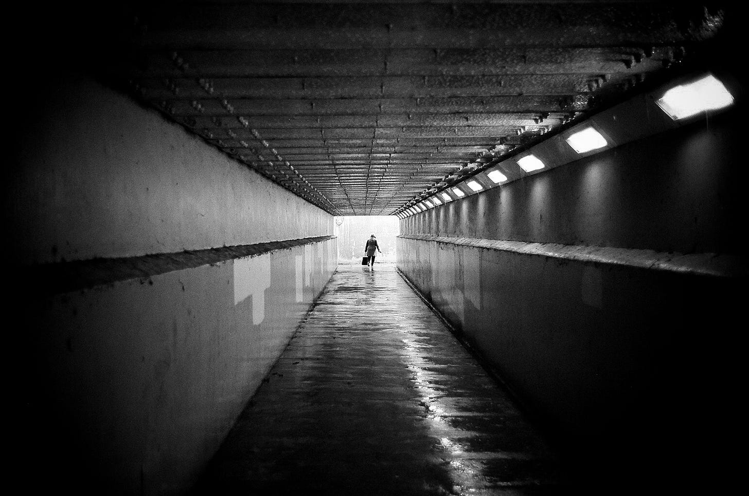 A black and white photo of a lady walking down an underpass. I walk down this way every seek but can't remember taking this photo. 
