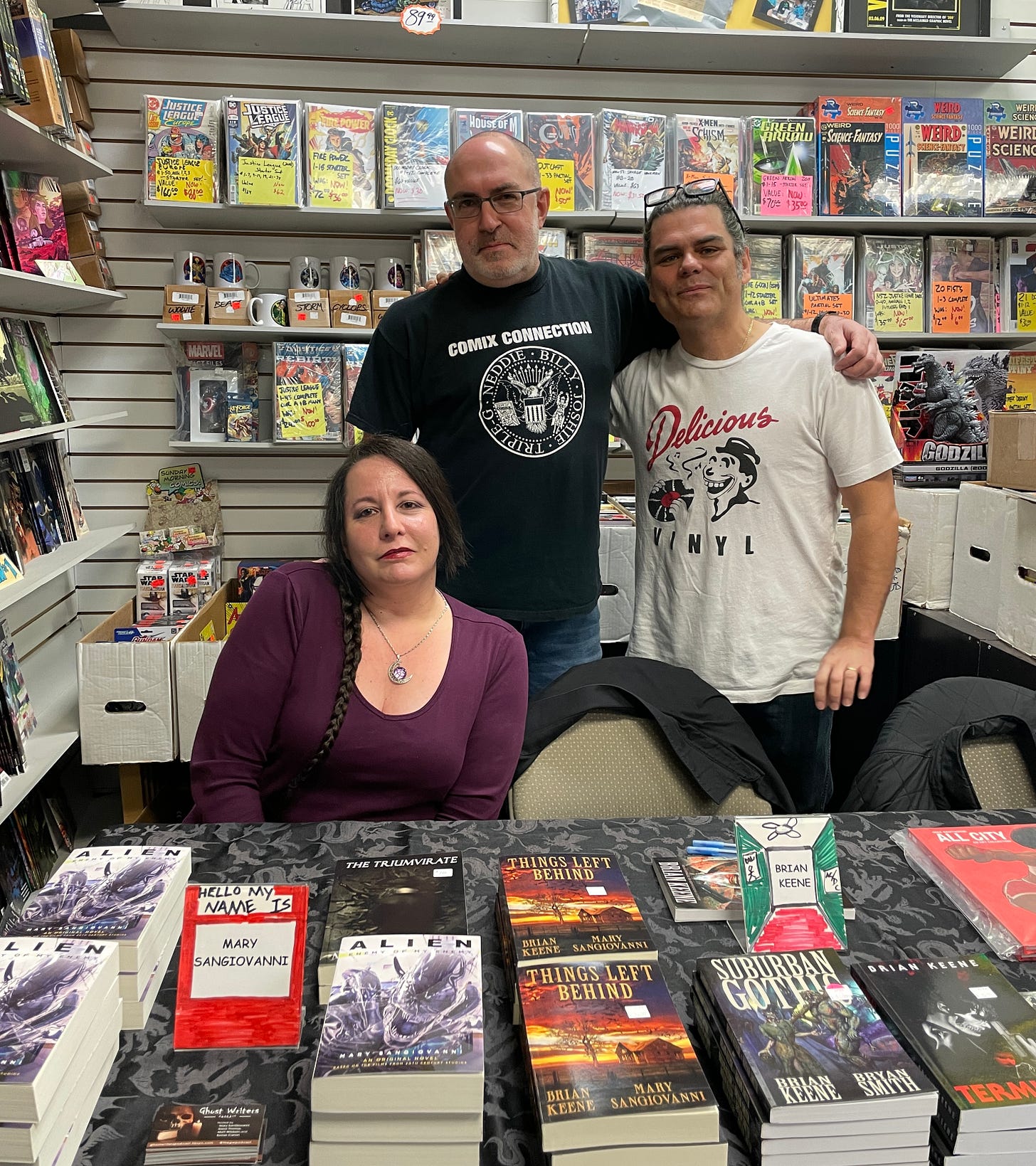 Mary SanGiovanni, Brian Keene, and Mike Hawthorne behind a table full of their books and comics.