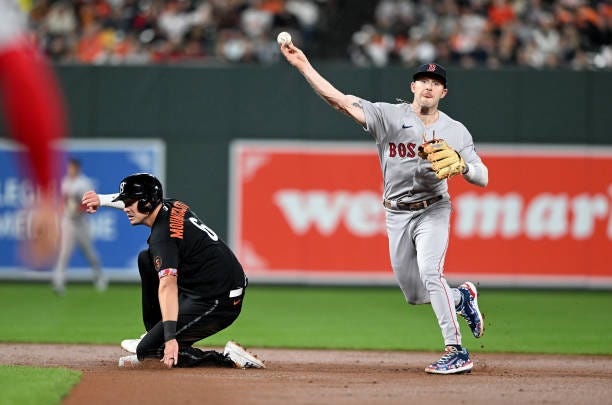 Trevor Story of the Boston Red Sox throws the ball to first base after forcing out Ryan Mountcastle of the Baltimore Orioles at second base in the...