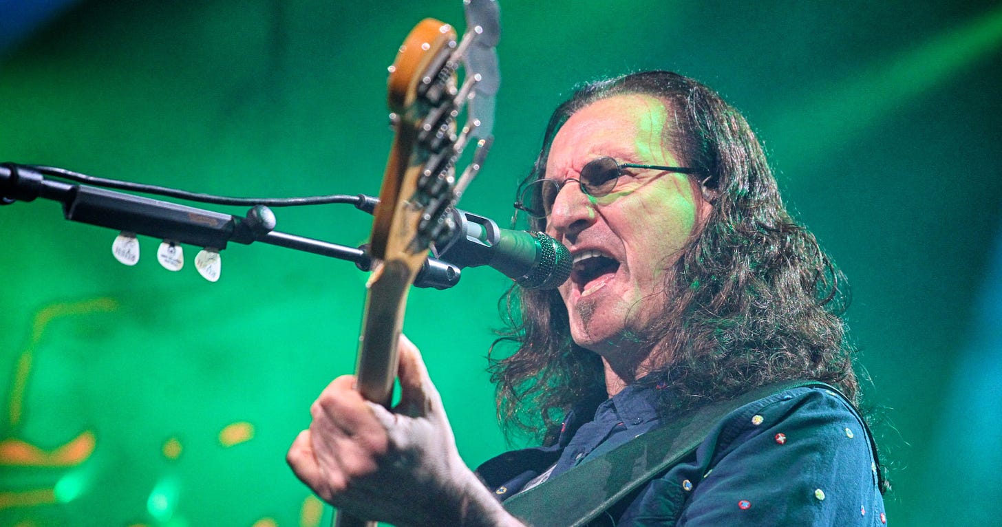 Geddy Lee of Rush playing bass and singing into a microphone on stage.