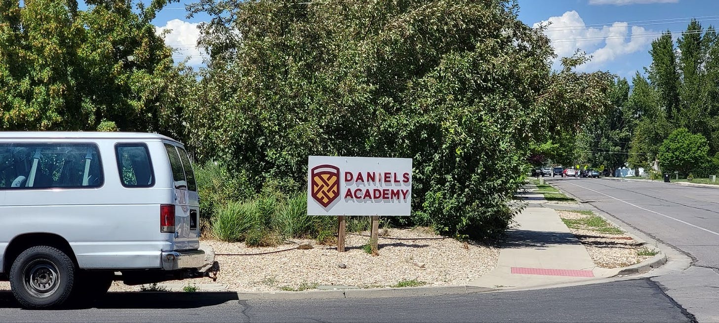 A sign on a streetcorner with "DANIELS ACADEMY" printed in red letters