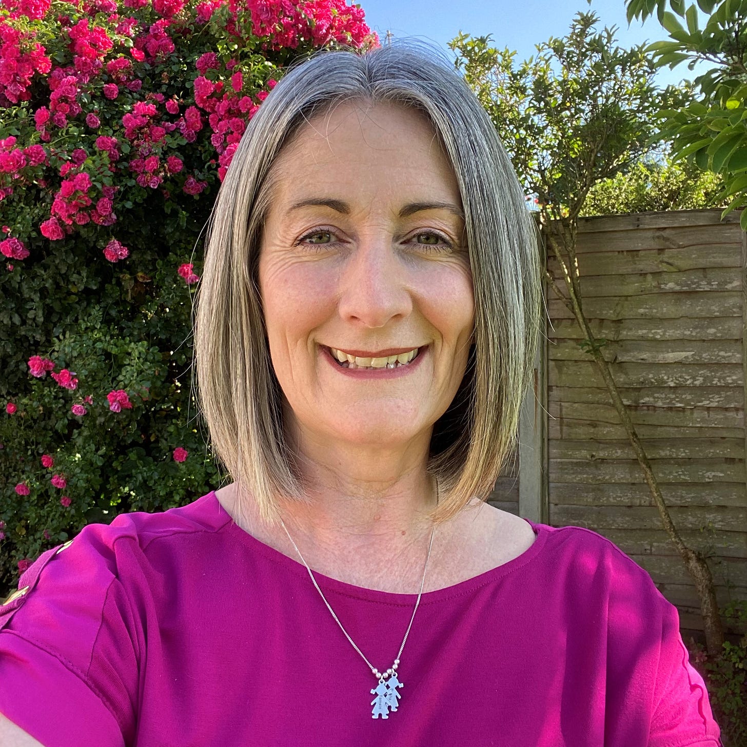 head and shoulders of Steph, grey haired 51 year old mum wearing pink top and smiling