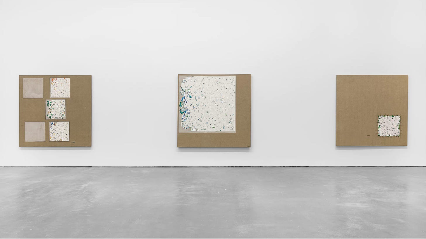 Installation view of Robert Ryman: 1961-1964 at David Zwirner Gallery. Three paintings hung on the wall all share a square format and bare linen background. Each has also has a square area or areas which are covered in oil brushstrokes in layers, with colored layers, mostly greens, partly obscured by white brushstrokes on top. 