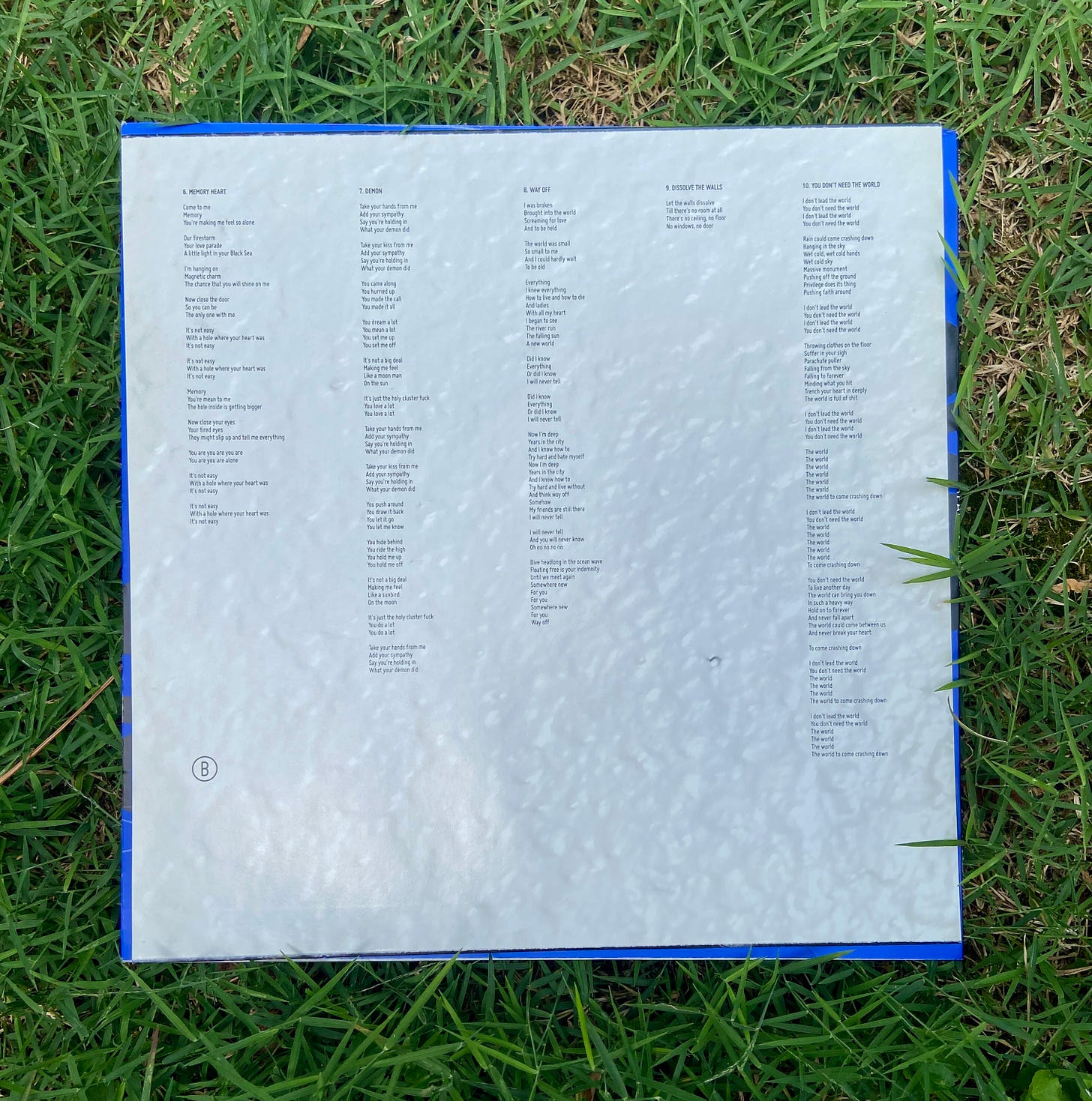 the inside jacket of the vinyl side B has lyrics and an image of a textured white wall and sits on top of bright green grass.