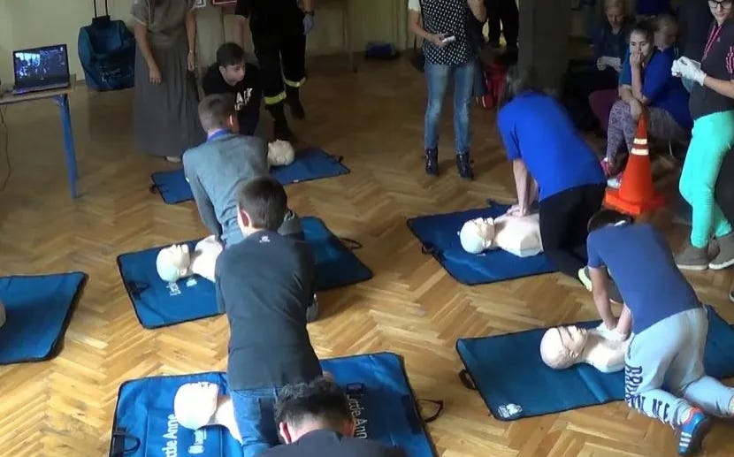 A group of people practicing CPR on mannequins in a training room, learning essential first-aid skills as part of a community defense initiative.