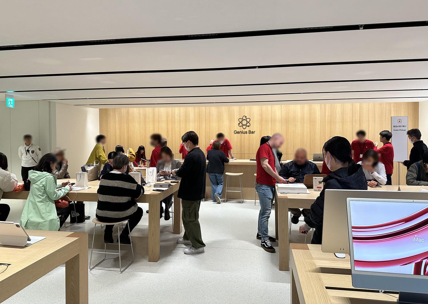 The upper level of Apple Shinsaibashi. A large Genius Bar with a wood back wall spans the far side of the store.