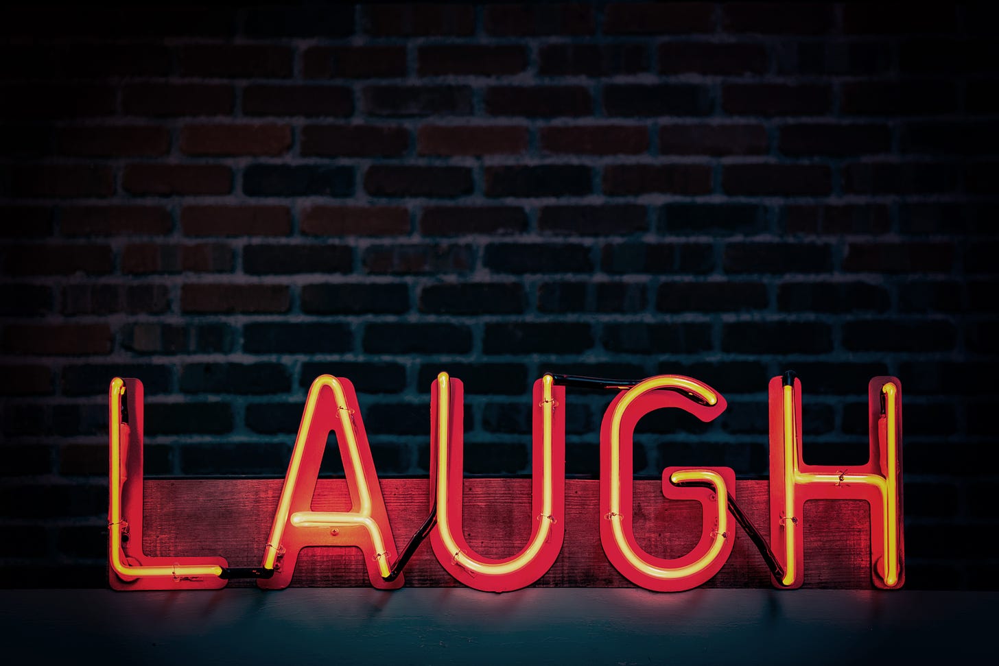 A red neon sign reads "laugh" against a dimly lit red, brick wall