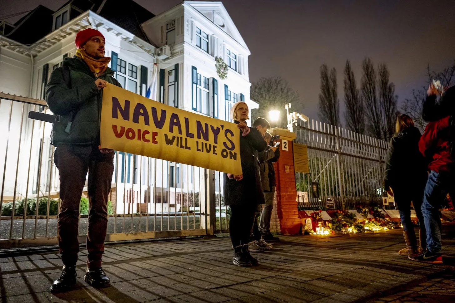 People gather outside the Russian Embassy in The Hague holding a sign in tribute of late Russian opposition leader Alexei Navalny.