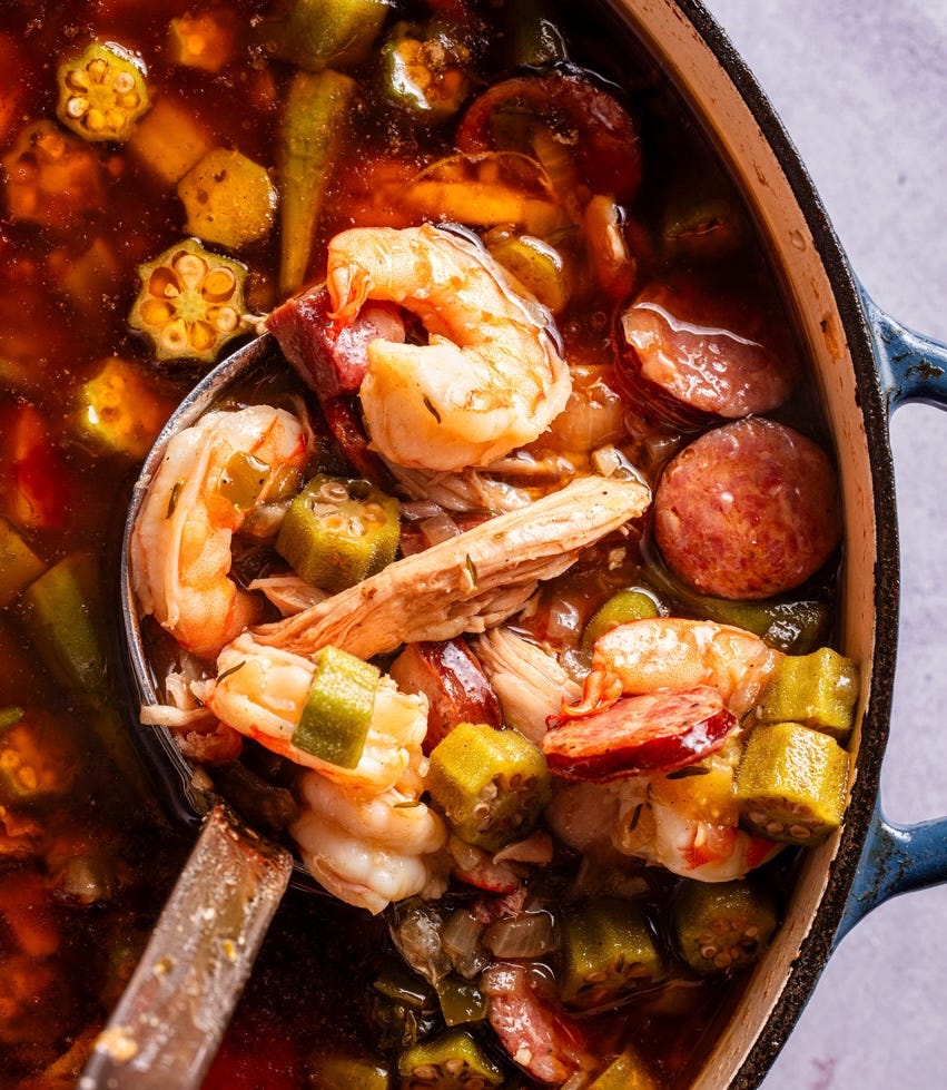 spoon pulling out from a dutch oven of gumbo with shrimp and sausage