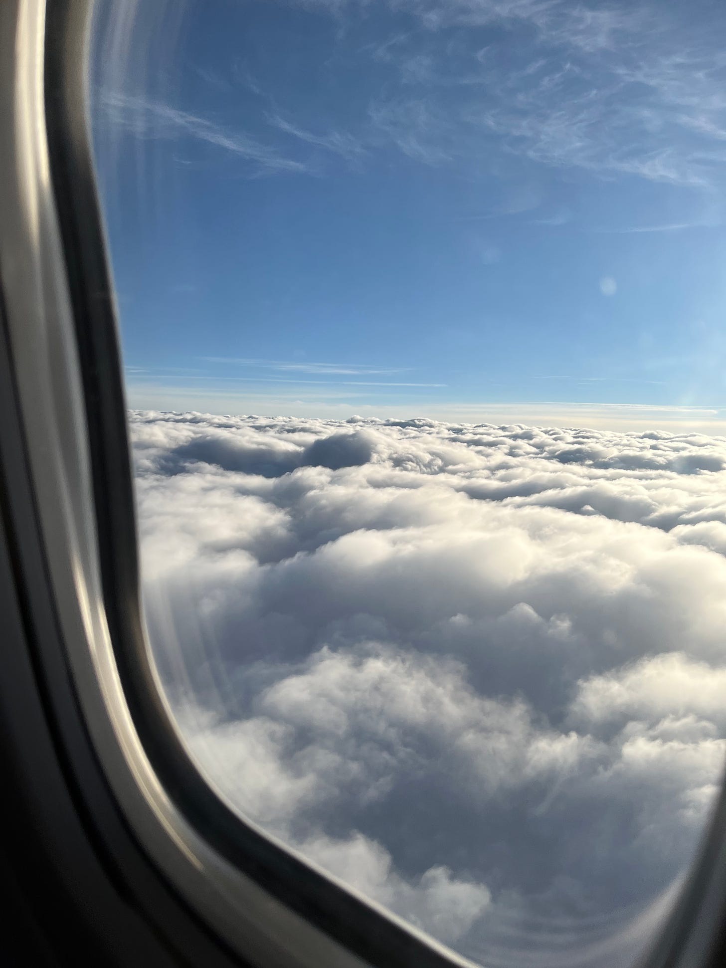 Picture taken of window in airplane, showing blue sky and clouds