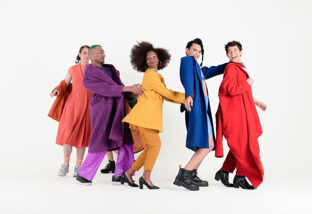 Young LGBT adults wearing rainbow clothing make silly faces while dancing in a line 